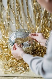 Hands decorating a shimmering disco ball with golden celebration decorations.